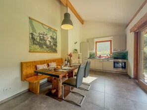 A dining area with a wooden bench and table, a painting above, and a kitchen with modern appliances. - Chalet with sauna near the Nassfeld region (Hermagor-Pressegger See)