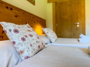A hotel room with a wooden headboard, two beds with floral-patterned pillows, and a door in the background. - Chalet with sauna near the Nassfeld region (Hermagor-Pressegger See)