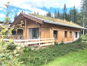 Une cabane en bois avec un toit en pente, une terrasse en bois et une fenĂȘtre ornĂ©e dâune serviette verte.