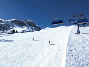 A ski slope with skiers, a chairlift, and snow-covered mountains.