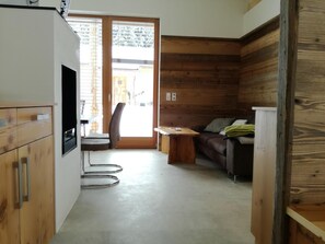 A compact room with a wooden wall, a sofa, a small table, and a chair. - Chalet with infrared sauna for mindful vacation (Hermagor-Pressegger See)