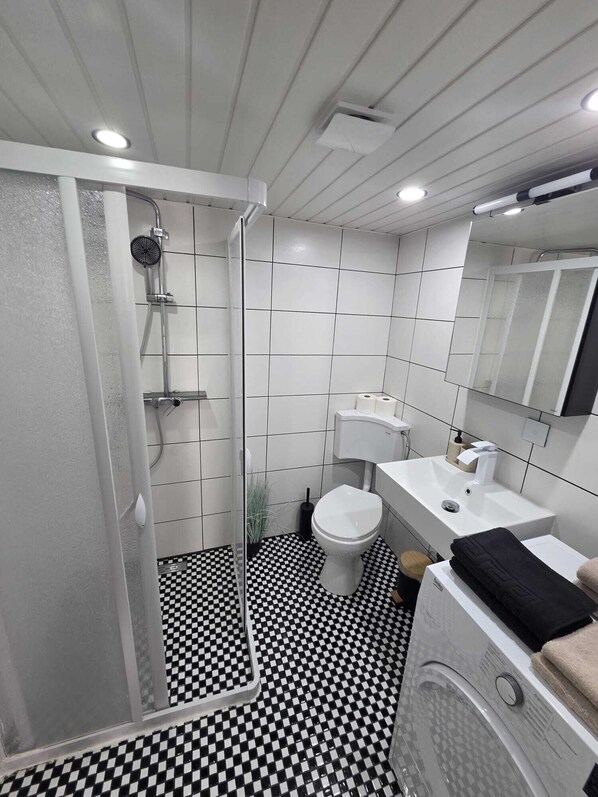 Un bagno con doccia, WC, lavandino e pavimento a scacchi.