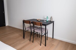 Ein Essbereich mit einem schwarzen Tisch, zwei Holzsesseln, einer kleinen Schüssel, einem Glas, einer Flasche und einer Vase.