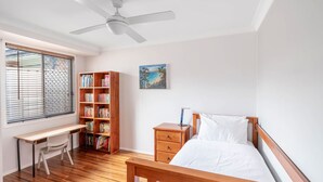 Ein Schlafzimmer mit Bett, Schreibtisch, Bücherregal, Nachttisch und Deckenventilator.