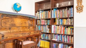 Ein Zimmer mit einem Holzpiano, einem Bücherregal voller Bücher und einem Globus an der Wand.