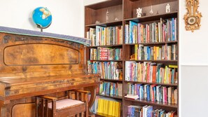 A room with a wooden piano, a bookshelf filled with books, and a globe on the wall. - Urban Tranquility a family home (Wollongong)