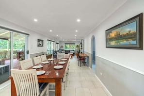 A dining area with a long table, chairs, and a view of greenery outside.