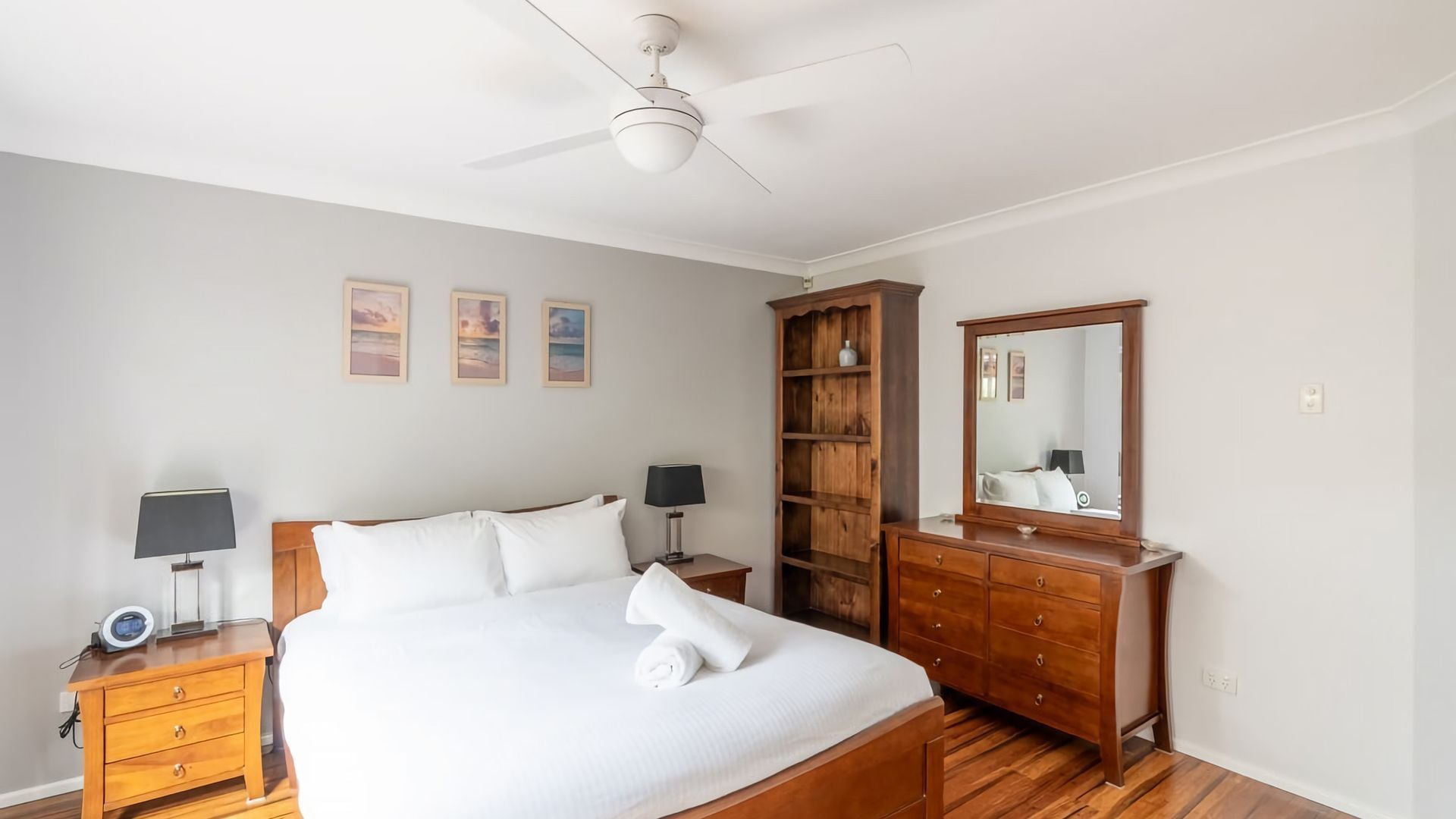 A bedroom with a bed, bedside tables, a wardrobe, a ceiling fan, and wall-mounted artwork.