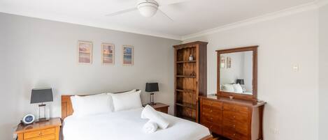 A bedroom with a bed, bedside tables, a wardrobe, a ceiling fan, and wall-mounted artwork.