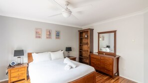 A bedroom with a bed, bedside tables, a wardrobe, a ceiling fan, and wall-mounted artwork.