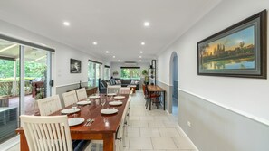 A spacious dining area with a long table set for six, a sofa, and a painting on the wall. - Urban Tranquility a family home (Wollongong)