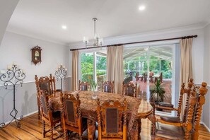 A dining room with a large wooden table and chairs, a chandelier, and a view of the outdoors.