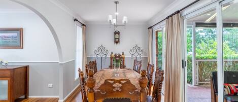 A dining area with a wooden table and chairs, a chandelier, and a view of greenery outside.