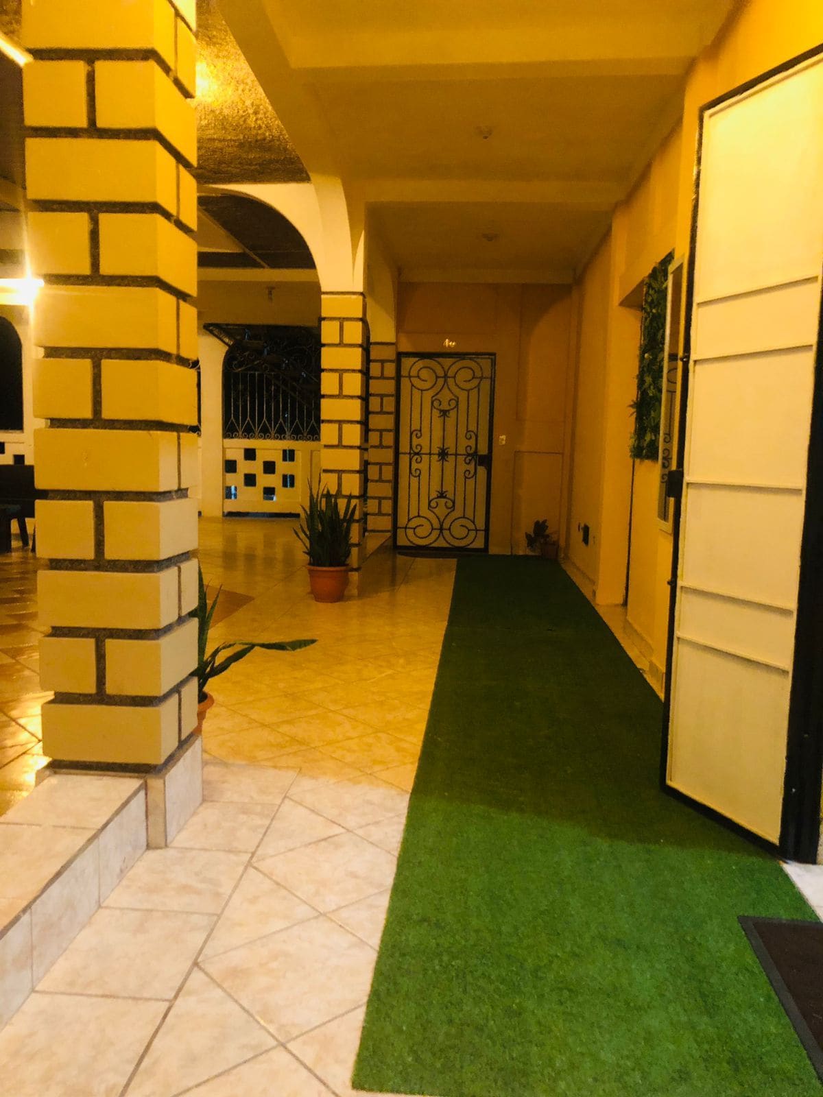 Un pasillo con alfombra verde, piso de baldosas, pared de ladrillo y una reja metálica.