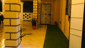 Un pasillo con alfombra verde, piso de baldosas, pared de ladrillo y una reja metálica.