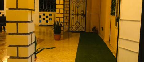 A hallway with a green carpet, a tiled floor, a brick wall, and a metal gate.