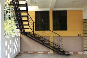 Un escalier orné de rampes en métal ouvragé, un mur jaune et une fenêtre avec des barreaux noirs.