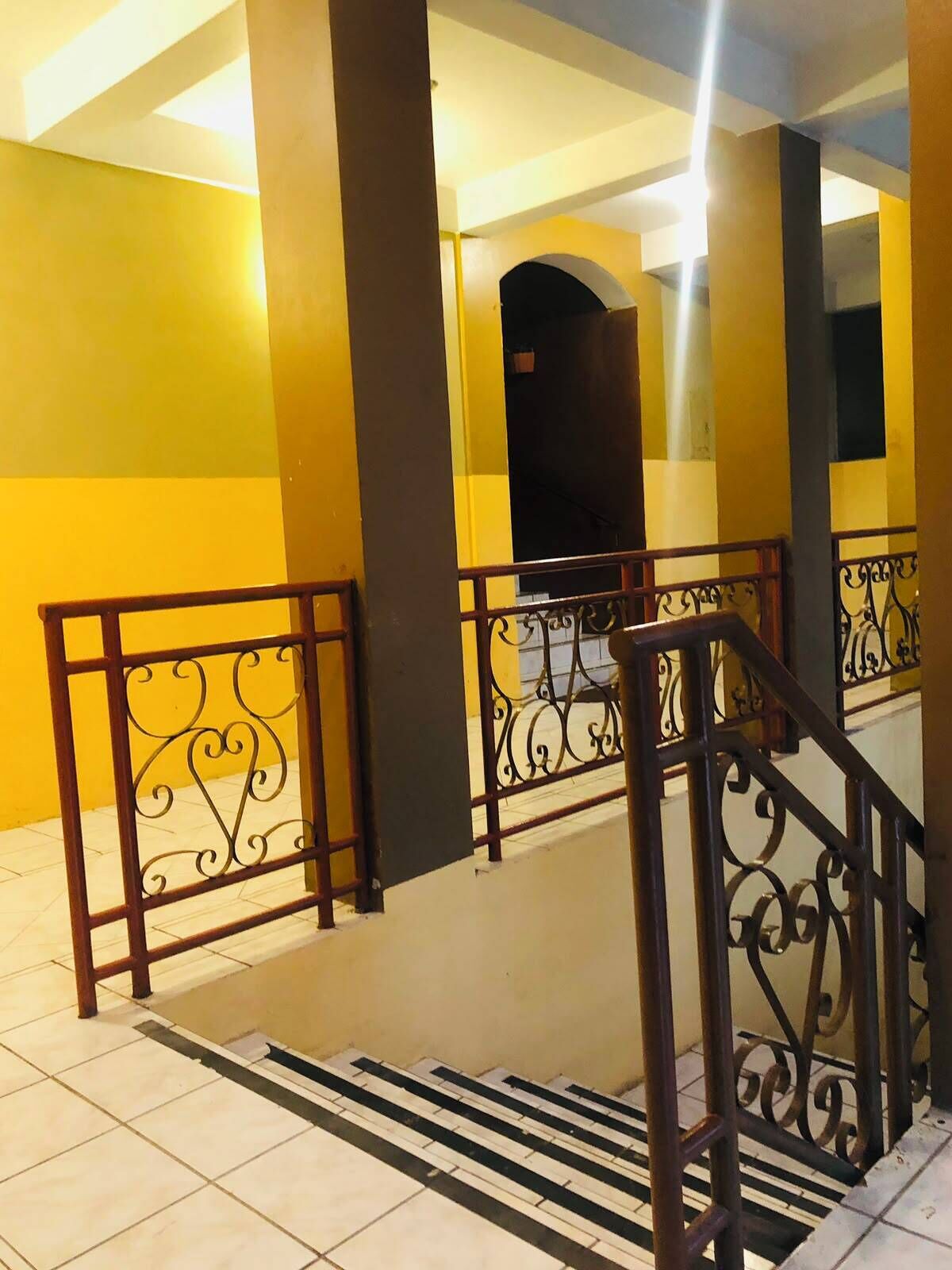 A staircase with metal railings and a tiled floor, leading to an upper level with yellow walls and a dark archway.