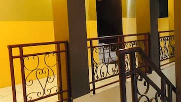 A staircase with metal railings and a tiled floor, leading to an upper level with yellow walls and a dark archway.