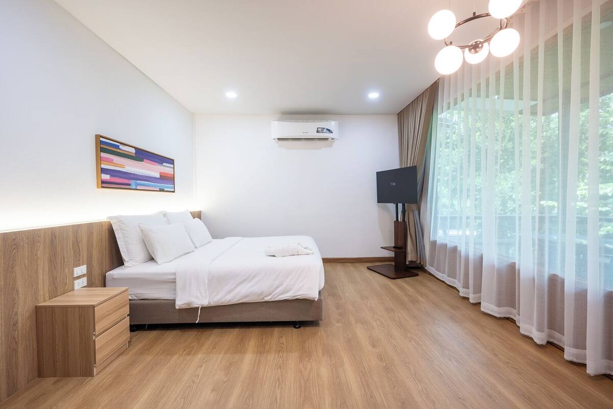 Una habitación de hotel moderna con cama, televisión, aire acondicionado y ventana con cortinas.