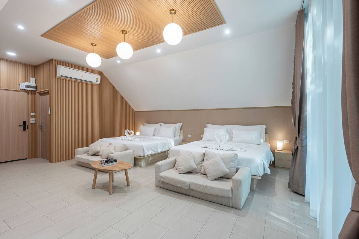 A modern hotel room with two beds, a sofa, a coffee table, and an air conditioning unit.