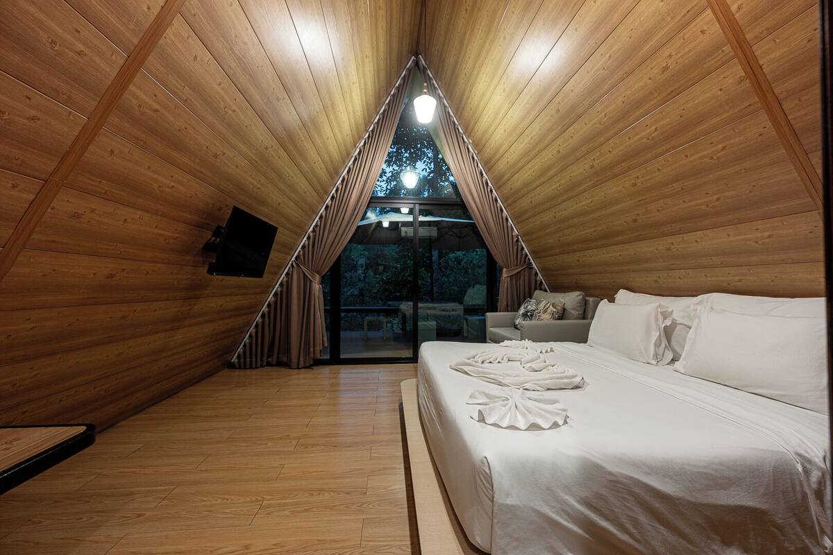 A cozy, triangular wooden room with a bed, a TV, and a view of the outdoors.