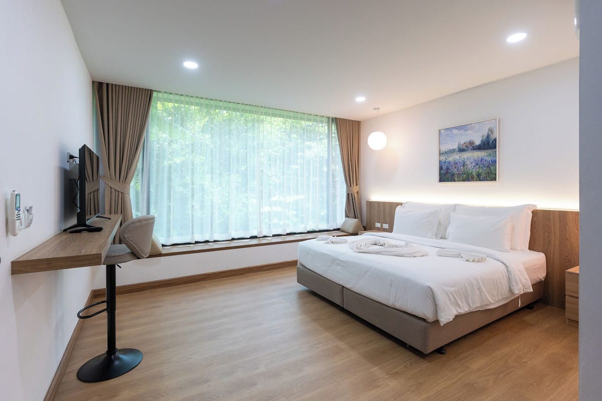 A hotel room with a bed, a desk, a chair, a TV, and a window with curtains.