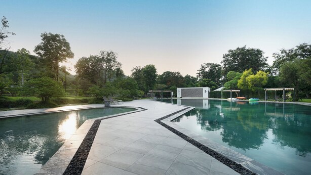 En swimmingpool med fliseterrasse, liggestole og en pergola.