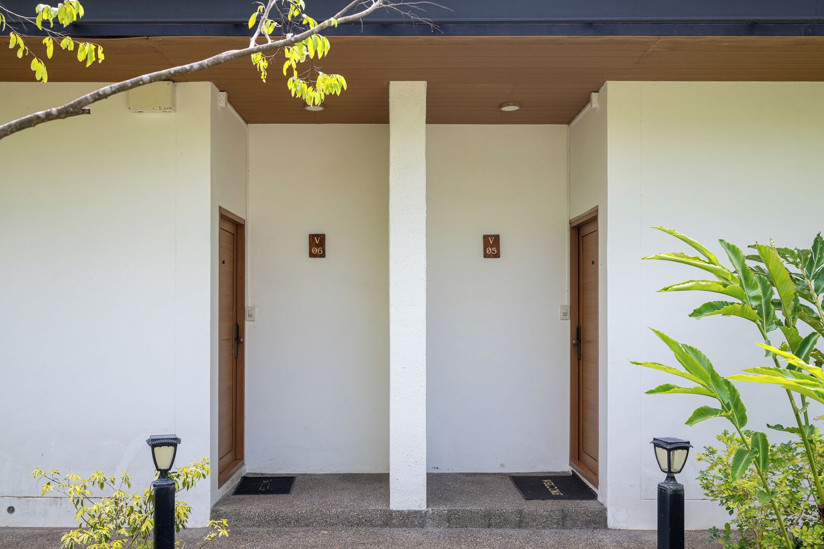 Een gebouwde ingang met twee deuren, elk voorzien van een nummer en een klein plantje aan de rechterkant.