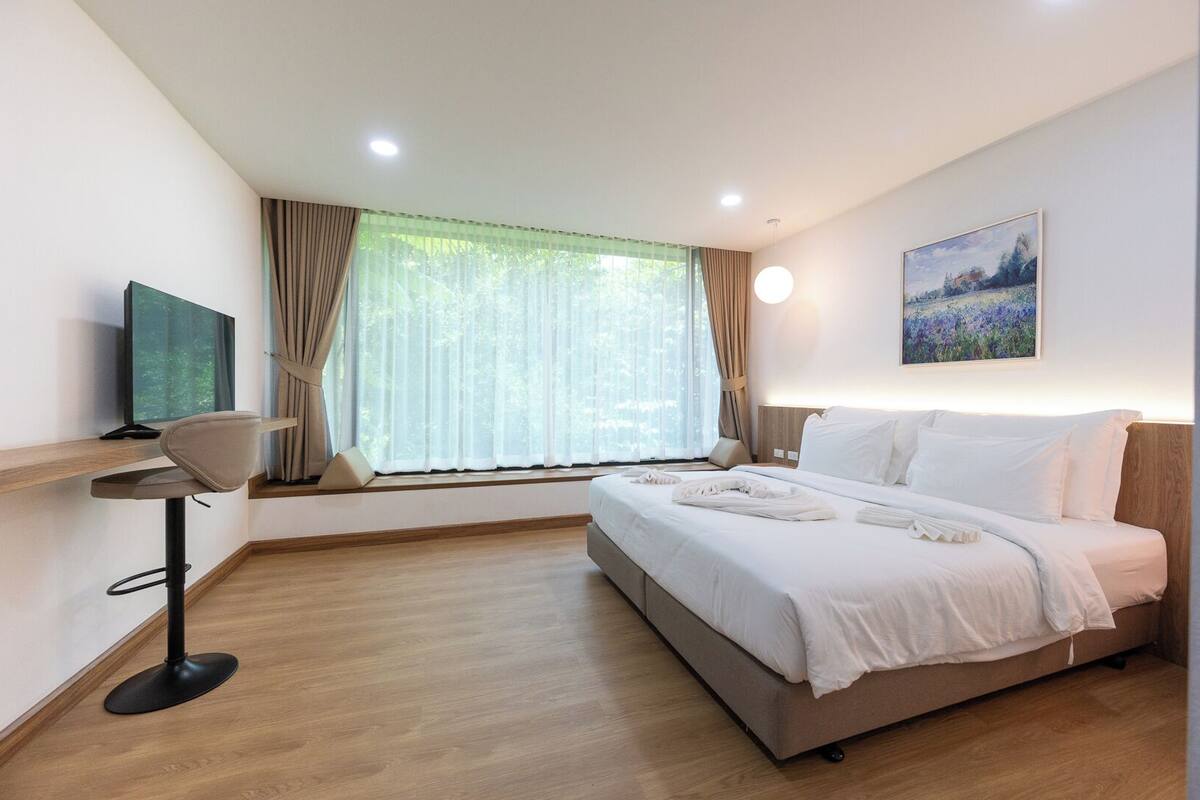 Una habitación de hotel con cama, televisión, escritorio y ventana con cortinas.