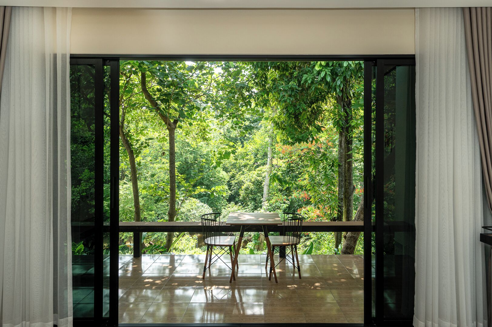 A dining area with a table and chairs, large windows, and a view of a forest.