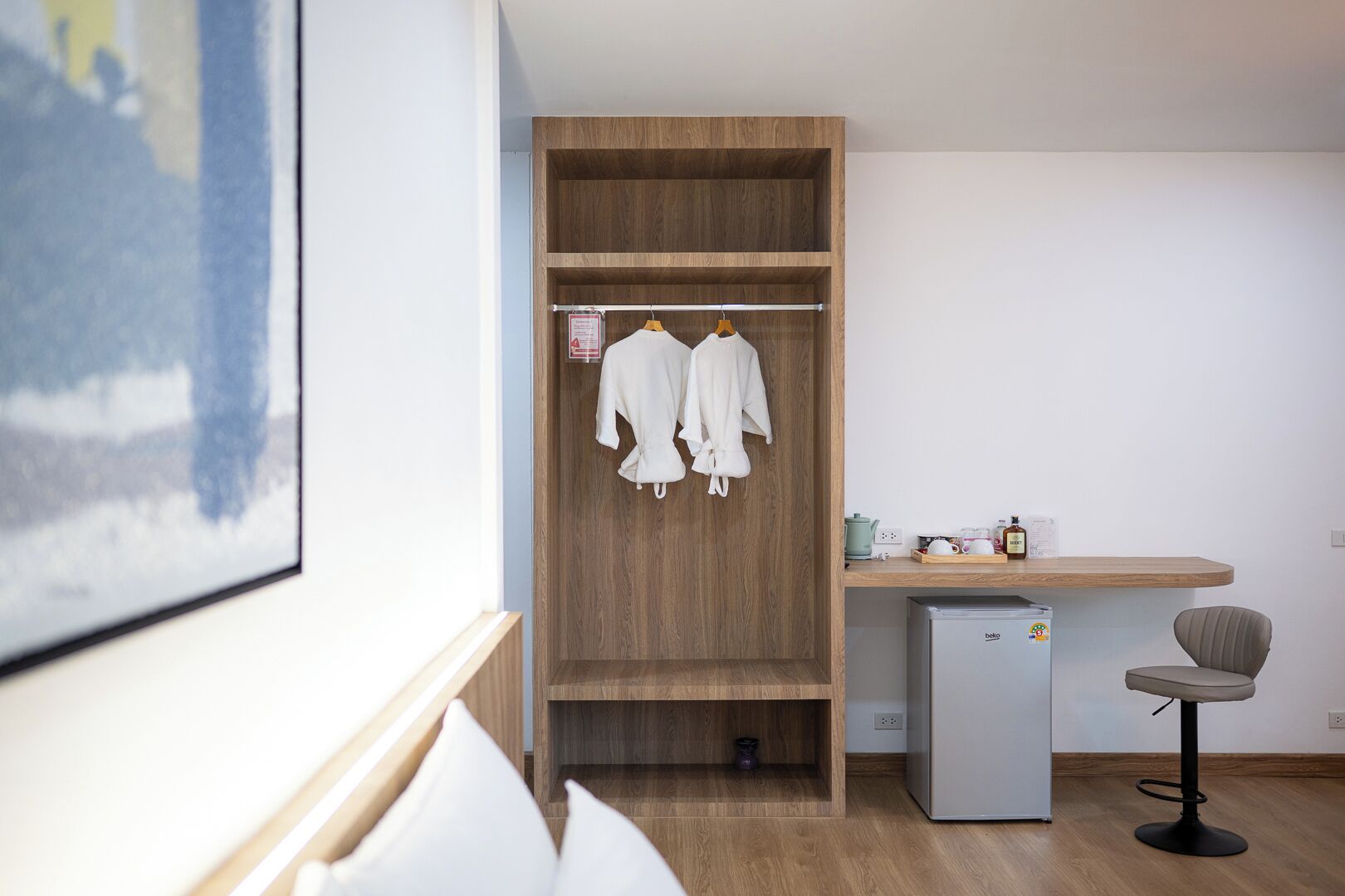 A modern room with a wooden wardrobe, a small kitchenette, a white sofa, and a grey chair.