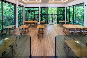 Un amplio comedor interior con grandes ventanales, mesas y sillas de madera.