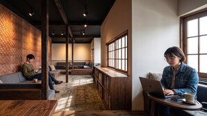 A cozy reading area with a fireplace, a seating area with a sofa and a table, and a large window providing natural light. - Pension Ruhe  (Kusatsu)