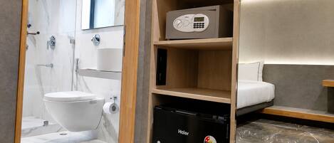 A compact bathroom with a toilet, a Haier refrigerator, and a shelf with a microwave.
