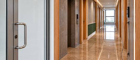 A modern hallway with a marble floor, wooden paneling, and a glass door with a handle.