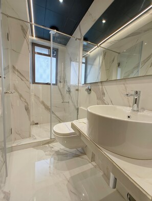 A modern bathroom with a glass-enclosed shower, a toilet, and a large sink with a mirror above. - Hotel Aston Residency (Kolkata)