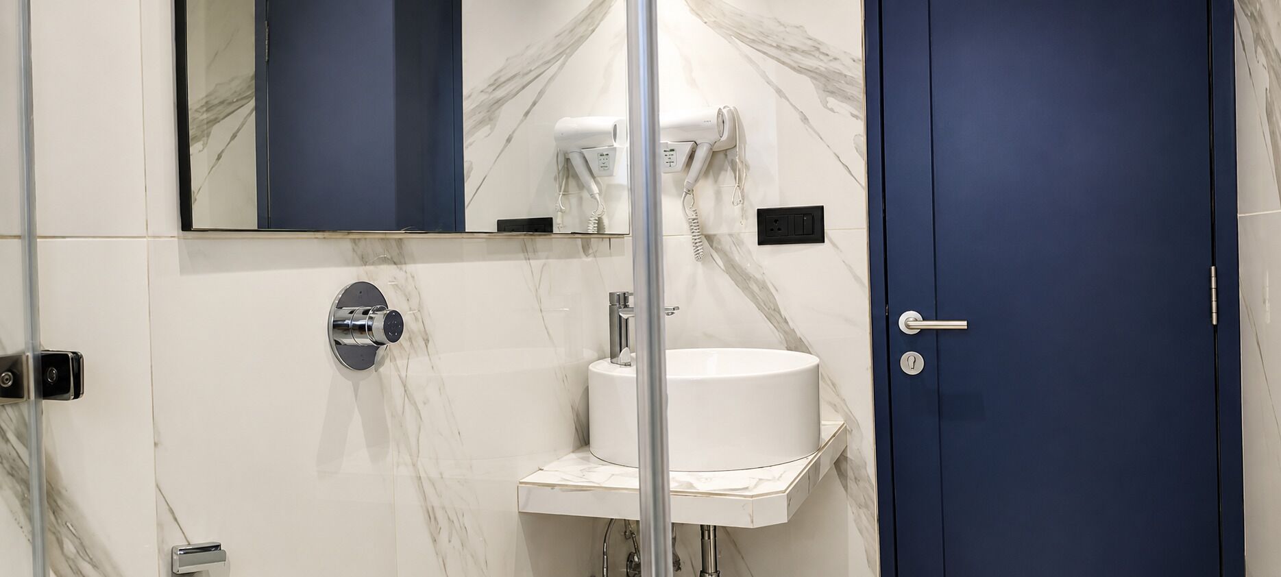 A bathroom with a marble wall, a white sink, a mirror, and a blue door.