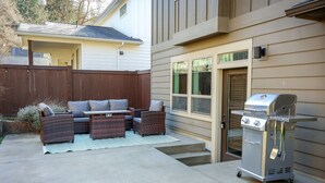 Un patio trasero con un conjunto de muebles, una parrilla y una casa.