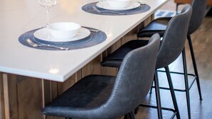 Un comedor con una mesa larga dispuesta para cuatro, sillas, un cuenco de limones y un televisor montado en la pared.