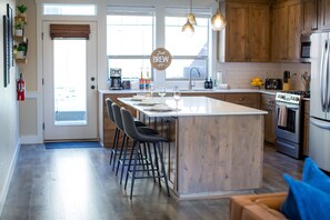 A kitchen with a central island, wooden cabinets, a built-in oven, and a microwave. - *NEW* 3 King beds, fenced yard, Firepit table (Spokane)