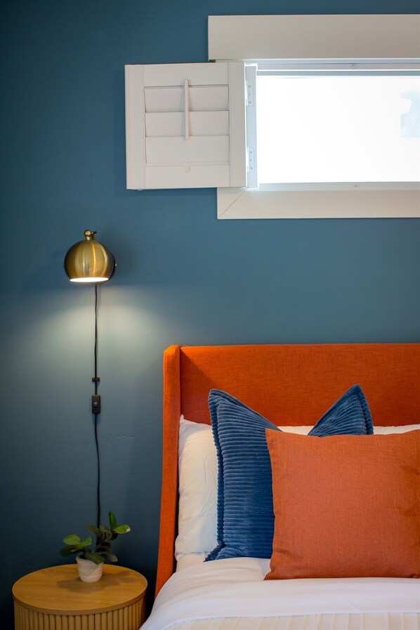 A bed with an orange headboard, a bedside lamp, and a window above the bed. - *NEW* 3 King beds, fenced yard, Firepit table (Spokane)