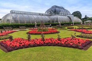 Uma estufa grande com estrutura em cúpula, rodeada por canteiros de flores bem cuidados e caminhos.