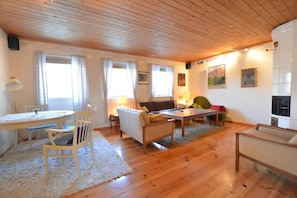 A cozy living room with wooden flooring, a sofa, a coffee table, a dining table with chairs, and a TV.