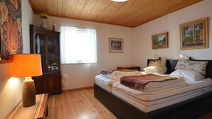Ein Schlafzimmer mit Holzboden, einem Bett mit Kissen und Decken, einem Nachttisch mit Lampe, einer Kommode und Wandbildern.
