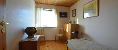Una habitación con techo de madera, una cama, un escritorio, una silla, un ventanal con cortinas y un cuadro en la pared.