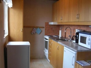 A compact kitchen with wooden cabinets, a built-in oven, a sink, and a microwave.