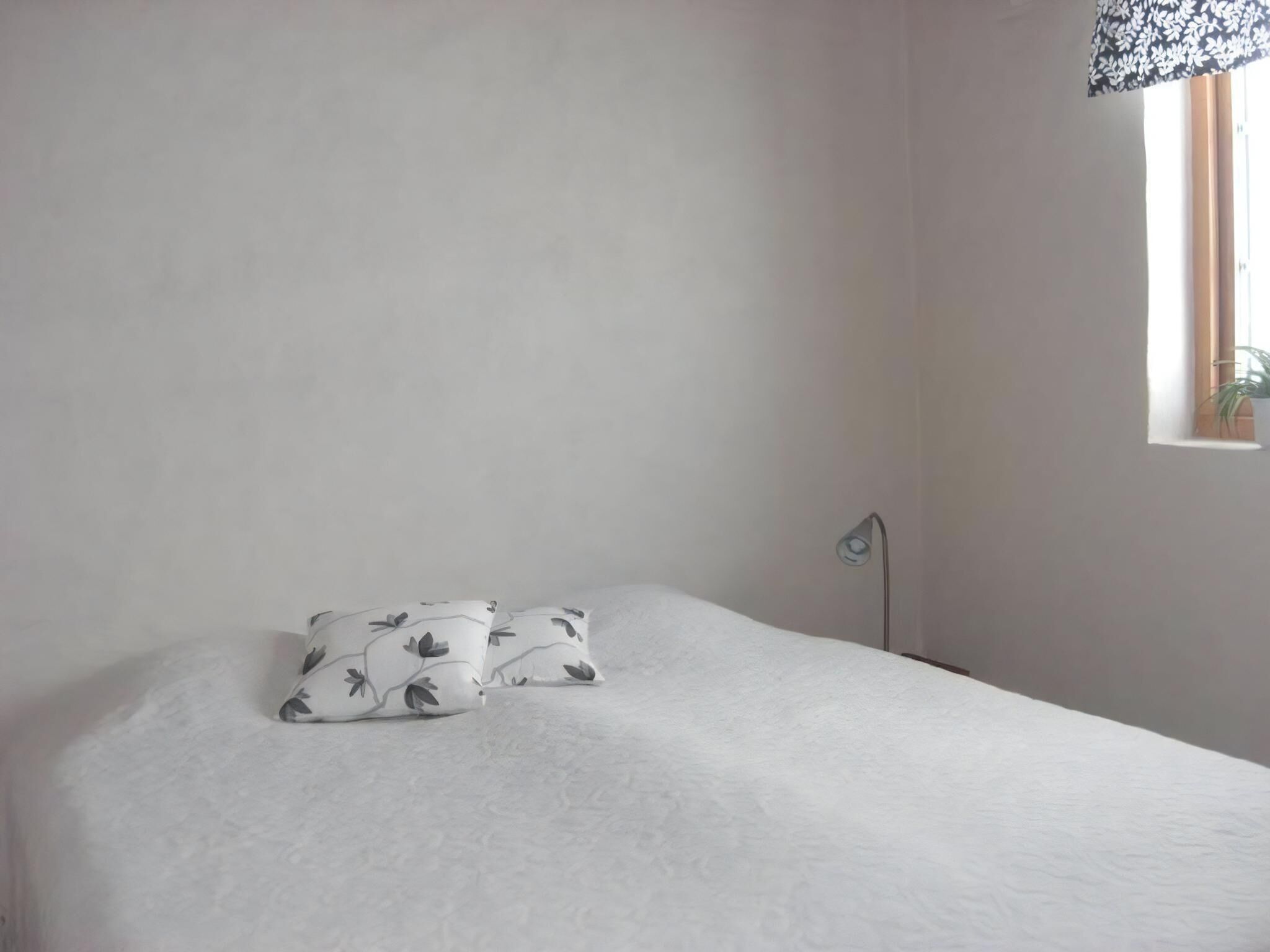 Une chambre à coucher avec un lit, deux oreillers, une lampe de chevet et une fenêtre avec une plante.