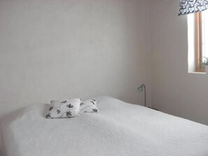 A bedroom with a bed, two pillows, a bedside lamp, and a window with a plant.