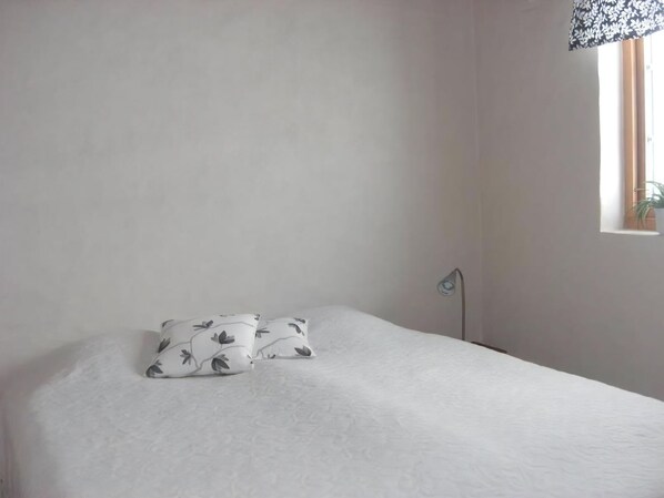 A bedroom with a bed, two pillows, a bedside lamp, and a window with a plant.